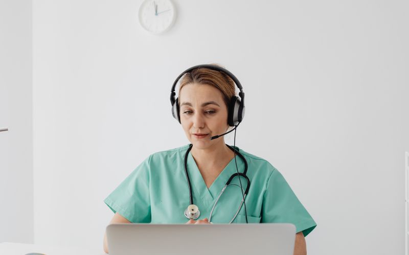 A nurse with a headset reviewing readings at a laptop